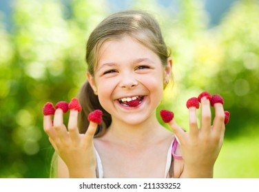 Young girl is holding raspberries on her fingers, outdoor shoot