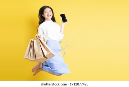 Young Girl Holding Shopping Bag With Cheerful Expression Jumping Up On Yellow Background