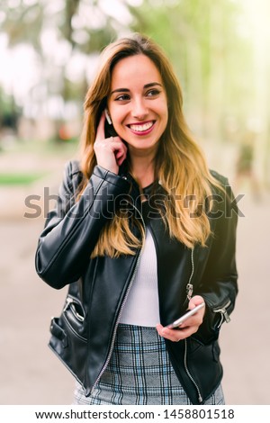 Young girl is holding a smartphone and listening to music on headphones or talk phone while walking in the park