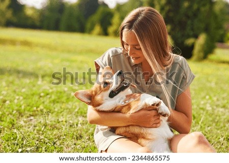 a young girl holds a cheerful and funny Welsh Corgi in her arms in a park in sunny weather, the concept of happy dogs