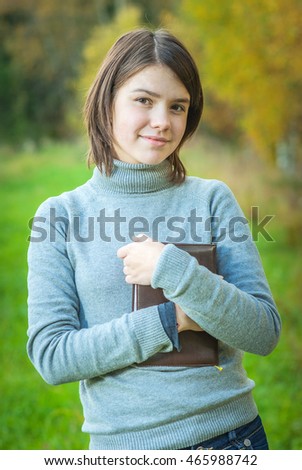 Young girl holds in hands book against autumn nature.