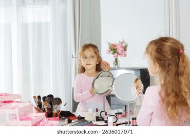 A young girl holds a makeup sponge as she looks into a mirror, with an array of make up brushes and cosmetics on the table in front of her