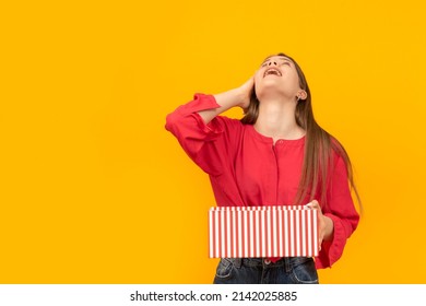 Young girl holds an open gift box in her hands and laughs with her head thrown back. Portrait on yellow background
