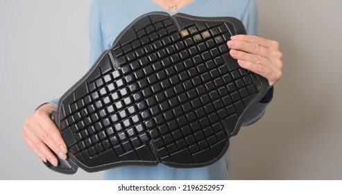 Young Girl Holds Plastic Back Protector From Motorcycle Jacket In Hands. Show Degree Of Bending. Camera Zoom Out Of The Texture Shield.