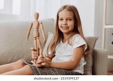 Young girl joyfully playing with a wooden mannequin on a comfortable couch, expressing creativity and imagination - Powered by Shutterstock