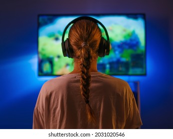 A young girl with a joystick in her hands sits in front of a large computer monitor and plays a video game. Neon light. Video games, hobbies, rest, relaxation. Shooting from the back. - Shutterstock ID 2031020546