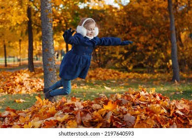 Young Girl Jumping Into A Pile Of Orange Leaves With Joy  And Pleasure In Autumn Park