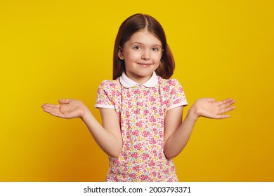 Young Girl Kid With Arms Out, Shrugging Her Shoulders, Saying Who Cares, So What, I Dont Know, Isolated Over Yellow Background