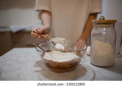 A young girl kneads dough for a chocolate cake, a pie. The girl adds a teaspoon of baking powder to the dough. Selectiv focus