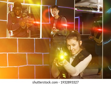 young girl with laser pistol playing laser tag with multinational team on dark labyrinth