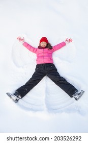 Young Girl Laying On Snow And Making Angel. Child Smiling And Spreading Hands And Feet