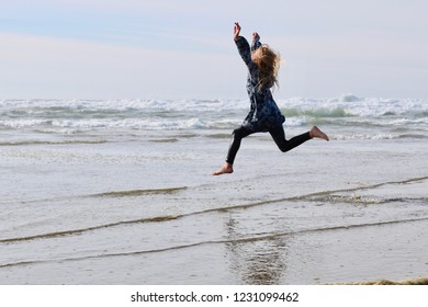 A Young Girl Leaping In Sheer Joy In The Waves On A Sandy Pacific Northwest Beach.