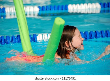 Young Girl Learning To Swim Using A Styrofoam Noodle In Community Swimming Pool