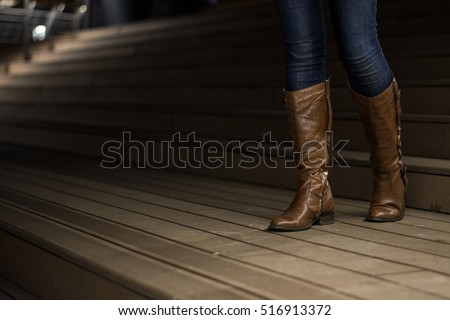 Young girl in leather boots walking down the wooden stairs