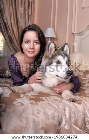 young girl in a lilac dress with her malamute in bed