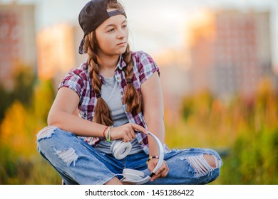 young girl listening music headphones, urban street style, outdoor street style hipster dj woman in black cap headphones dj listening to music and smiling, orange, crazy style city background, sunset
