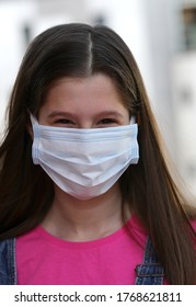 Young Girl With Long Black Hair As She Smiles Behind The Surgical Mask To Protect Herself From The Coronavirus During The World Epidemic