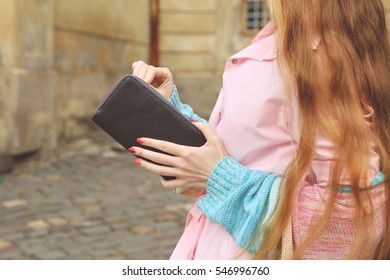 Young  Girl With Long Blond Hair In Soft Pink Dress And Knitted Pullover On The Streets. Woman With Dark Brown Wallet Or Clutch In Hands