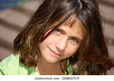 A Young Girl With Long Brown Hair And Green Eyes Looks Up At The Camera