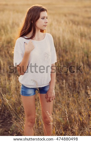 Young girl with long brown hair stay at the meadow and looks thoughtfully to right. Selective focus, warm tinted.