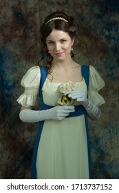 A young girl in a long dress of white and blue color. Looks directly at the camera. Holding white flowers. A woman in a retro dress. Historical reconstruction