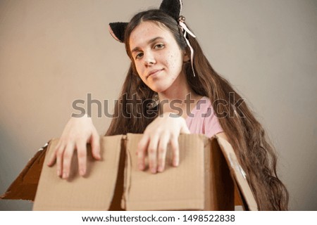 young girl with long hair looks out of large cardboard box. ears are fixed on hair of fantastic character. Cosplay, anime, fantasy
