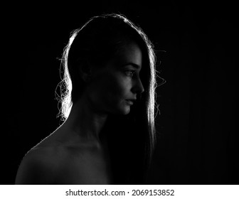 Young girl with long hair posing in backlight in a dark room. 