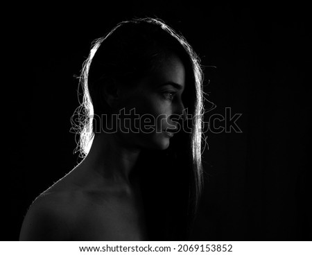 Young girl with long hair posing in backlight in a dark room. 