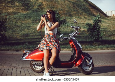 young girl with long hair in sunglasses in a black t-shirt tattoo on his shoulder in white pants with red lipstick posing on a retro scooter Vespa colors tiffany vintage style straw hat with a stylish