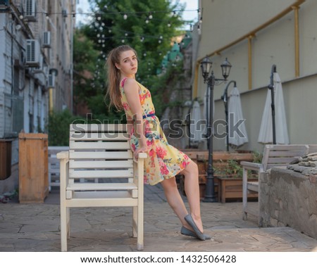 a young girl with long white curls in a dress walks through the old town in the summer. girl in a flowers dress with light curls. Beautiful blonde woman walking in yellow dress. Fashion summer photo.