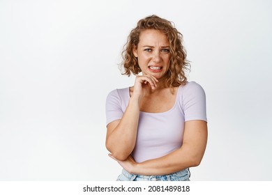 Young Girl Look At Cringe Scene, Grimacing And Staring With Dislike Or Disgust, Standing In Tshirt Over White Background