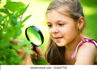 Young girl is looking at flower through magnifier, outdoor shoot