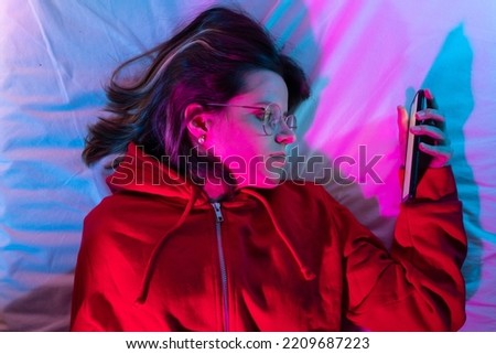 Young girl looking her smart phone doom scrolling on bed in the middle of the night with neon lights. Technology at bed concept.