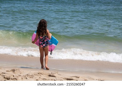 young girl looking at the massive ocean at seaside with a boogie board wearing one piece bathing suite