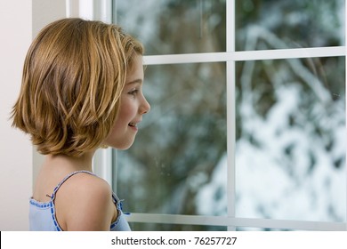 A Young Girl Looking Out The Window, Excited To See Snow Outside.