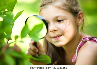 Young girl is looking at tree leaves through magnifier, outdoor shoot