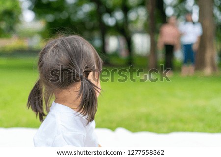 young girl looks back to her parent standing farway while she's plaing on the white mat in the garden.