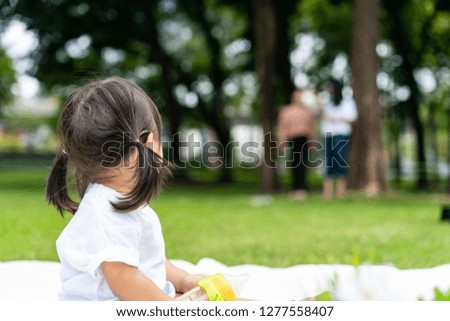 young girl looks back to her parent standing farway while she's plaing on the white mat in the garden.