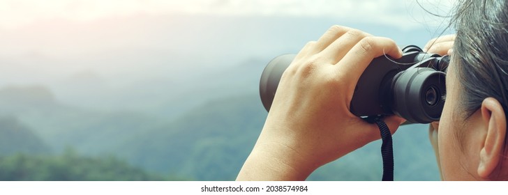 Young girl looks through binoculars on mountains background