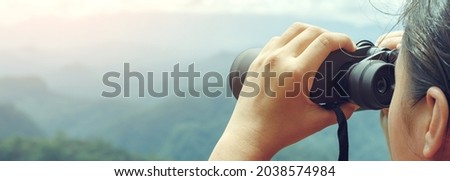 Young girl looks through binoculars on mountains background
