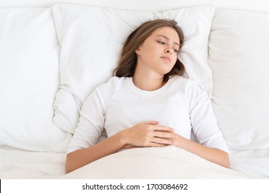 Young girl lying on bed dressed in white top, looking aside with bored and sad face, feeling worried, not willing to get up and go to studies or work - Shutterstock ID 1703084692