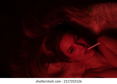 A young girl lying on the floor with a cigar in her mouth in dark room with red light