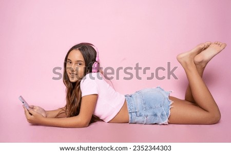 Young girl lying on floor and using smartphone isolated over pink background.