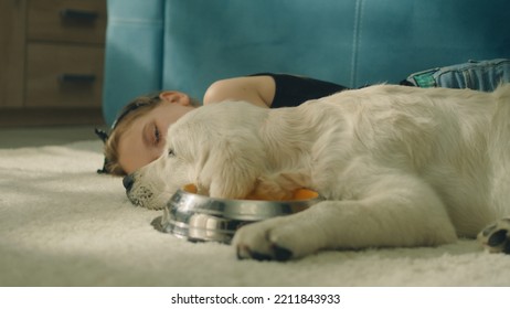 Young Girl Lying On Mild Carpet With Dog, Puppy Watching At Camera And Drinking Water, Chilling And Relaxing, Spending Leisure Time At Home. Golden Retriever.