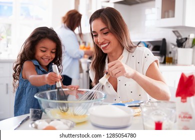 Young girl making cake in the kitchen with her mum, grandmother busy in background, selective focus - Powered by Shutterstock