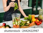 Young girl making green detox cocktail of fresh vegetables and fruits using blender in the kitchen. Healthy eating habits. Diet and vegetarianism for loosing weight and keep body fit