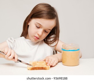 A Young Girl Is Making A Sandwich Consisting Of Wholemeal Bread And Peanut Butter.