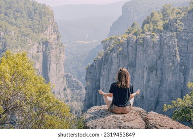 Young girl meditating in lotus yoga pose on top of the cliff overlooking scenic view of Tazi canyon in Turkey