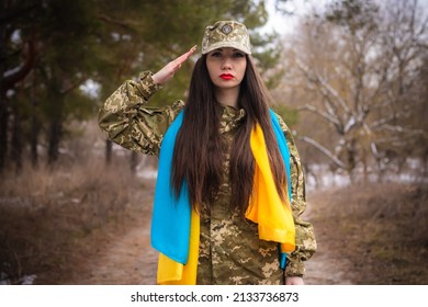 a young girl in military uniform salutes, on her shoulders the flag of Ukraine, serves in the army in the forest - Powered by Shutterstock