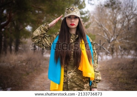 a young girl in military uniform salutes, on her shoulders the flag of Ukraine, serves in the army in the forest